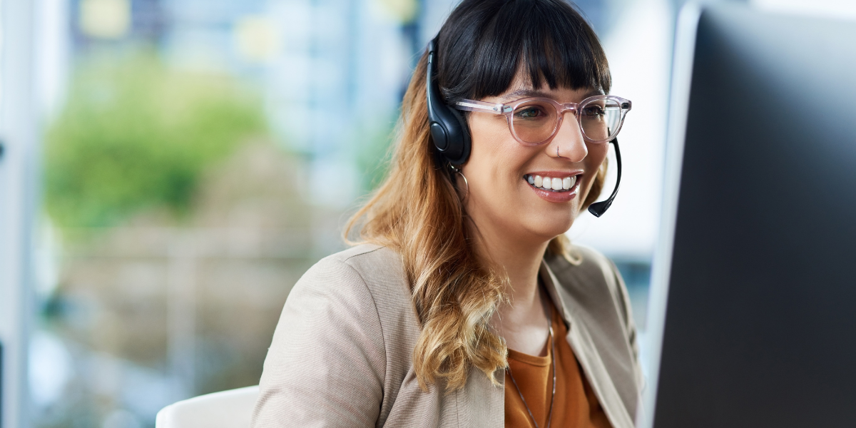 A dedicated Office Support professional in Cork, smiling while assisting clients over the phone at a well-organized desk. Launch your Office Support or Admin Career in Cork with Pitman Training.