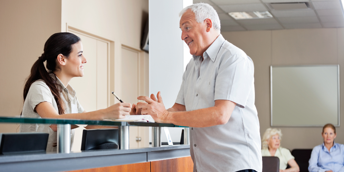 A dedicated medical secretary helps an elderly man check into his appointment, showcasing the essential patient-facing skills required to become a medical secretary in Cork.
