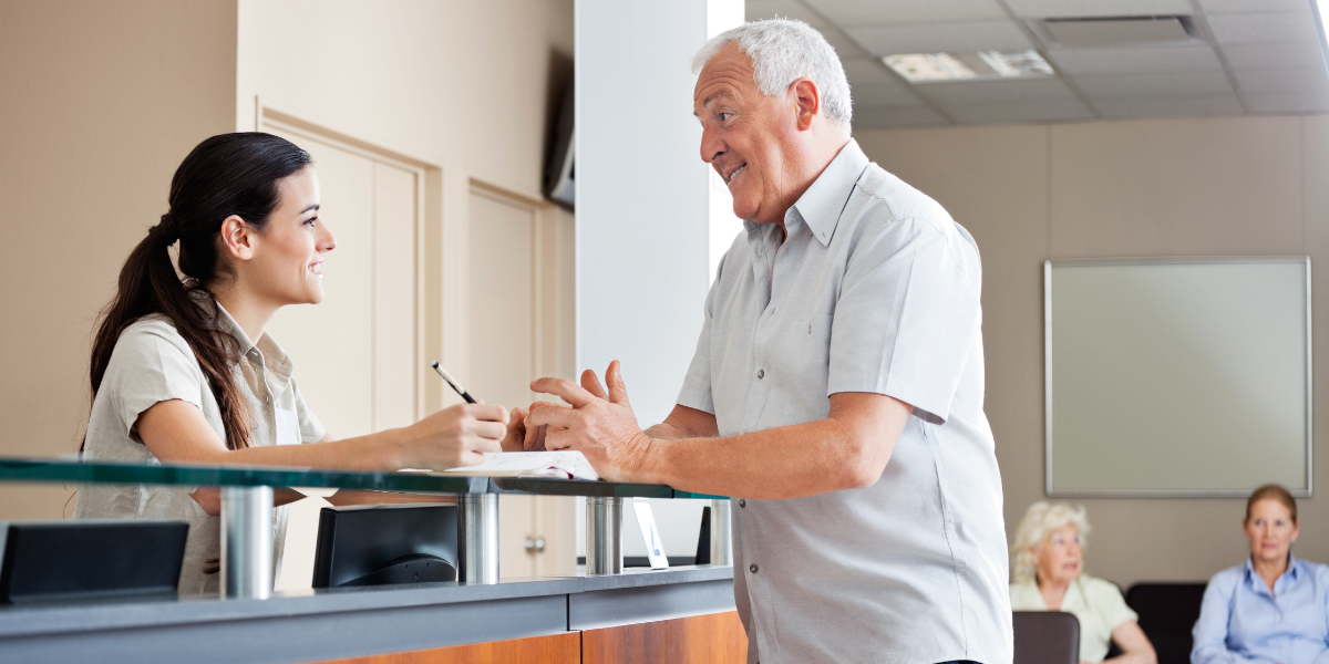 A friendly Medical Secretary in Wexford happily assisting a patient at the front desk, showcasing excellent customer service. Find Medical Secretary jobs in Wexford and start your journey.