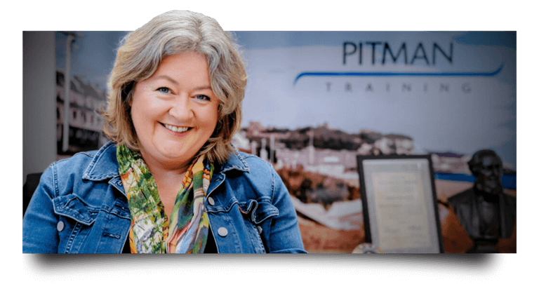 Portrait of Paula Elliott smiling warmly in a denim jacket and colorful scarf, with the Pitman Training logo and Dover coastline visible in the background, representing her 25-year journey as the successful owner of Pitman Training Dover.