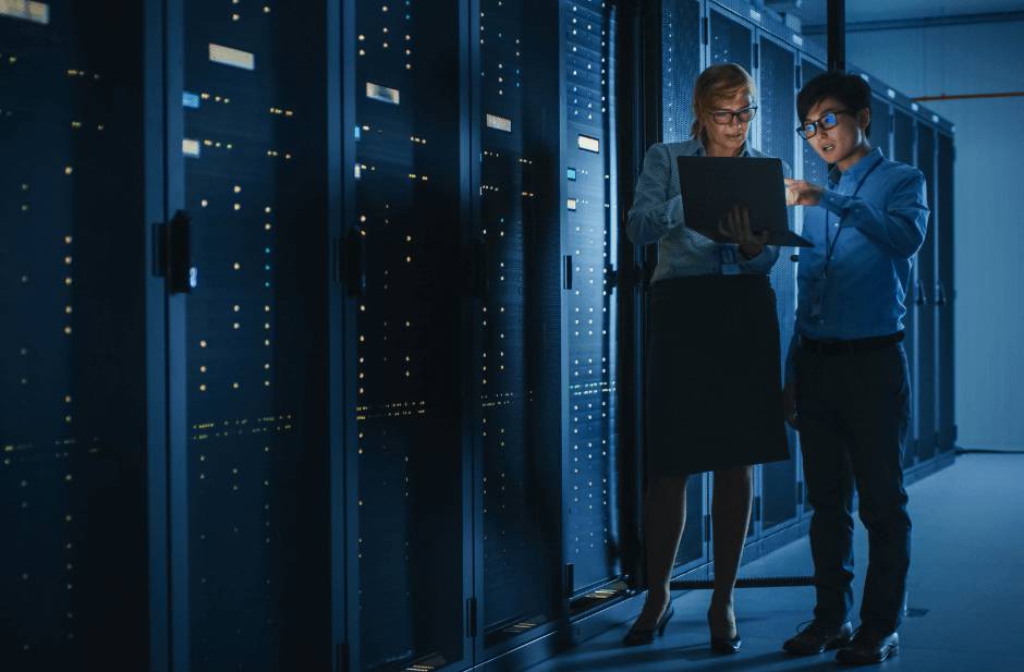 Two IT security professionals analysing data in server room during Pitman Training CompTIA Security+ diploma session.